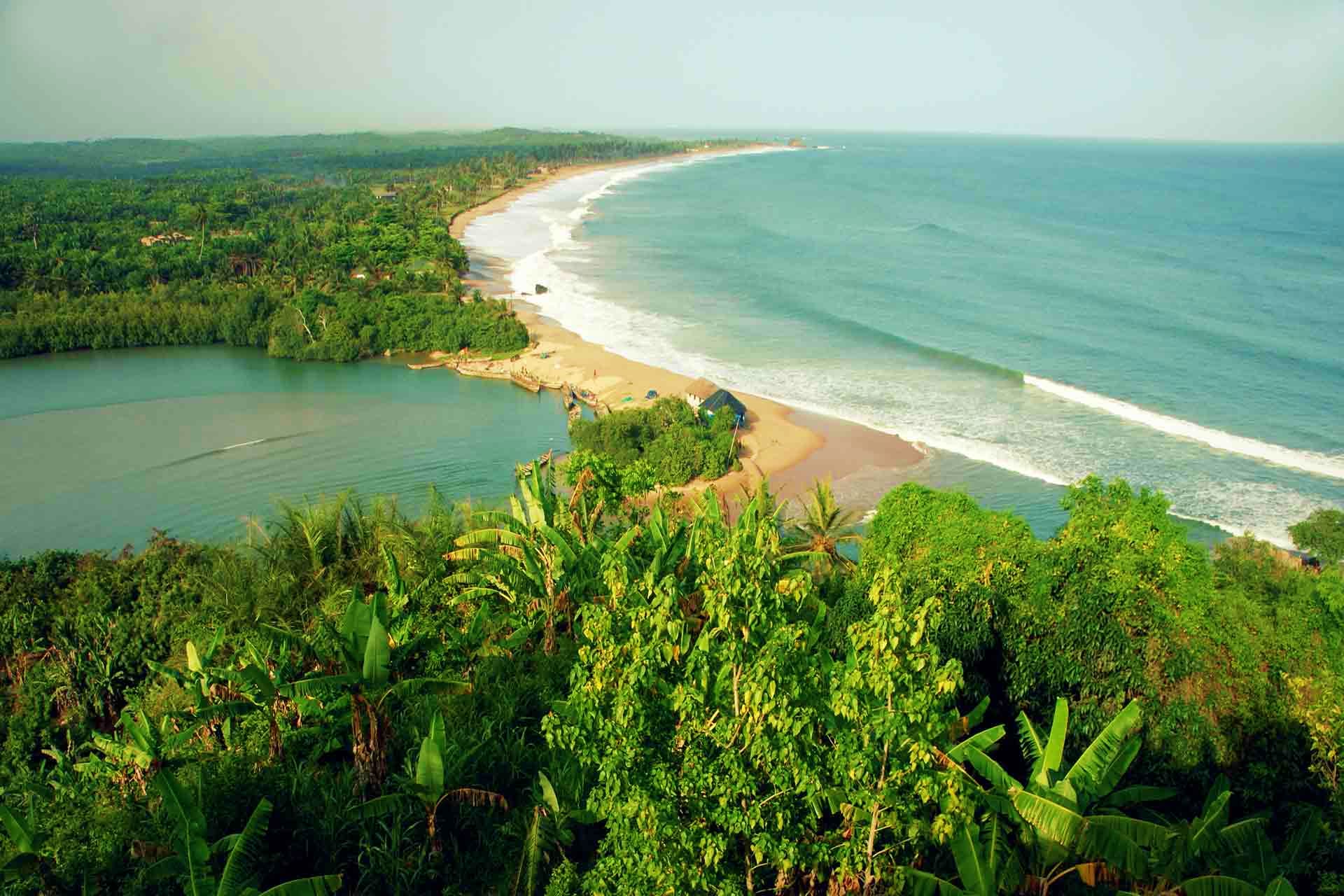 Ghana Visa Aerial view of Ghana's tropical coastline with golden sandy beach, turquoise ocean waves, dense palm forests, and lagoon